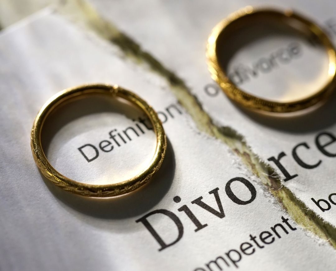 two wedding rings sitting on a divorce paper torn in half. 